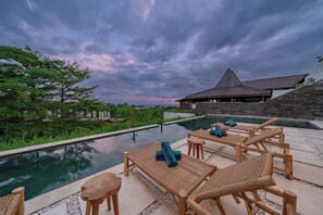An outdoor pool area with wooden lounge chairs and a stone building in the background. - Ocean Heritage (Kutuh)