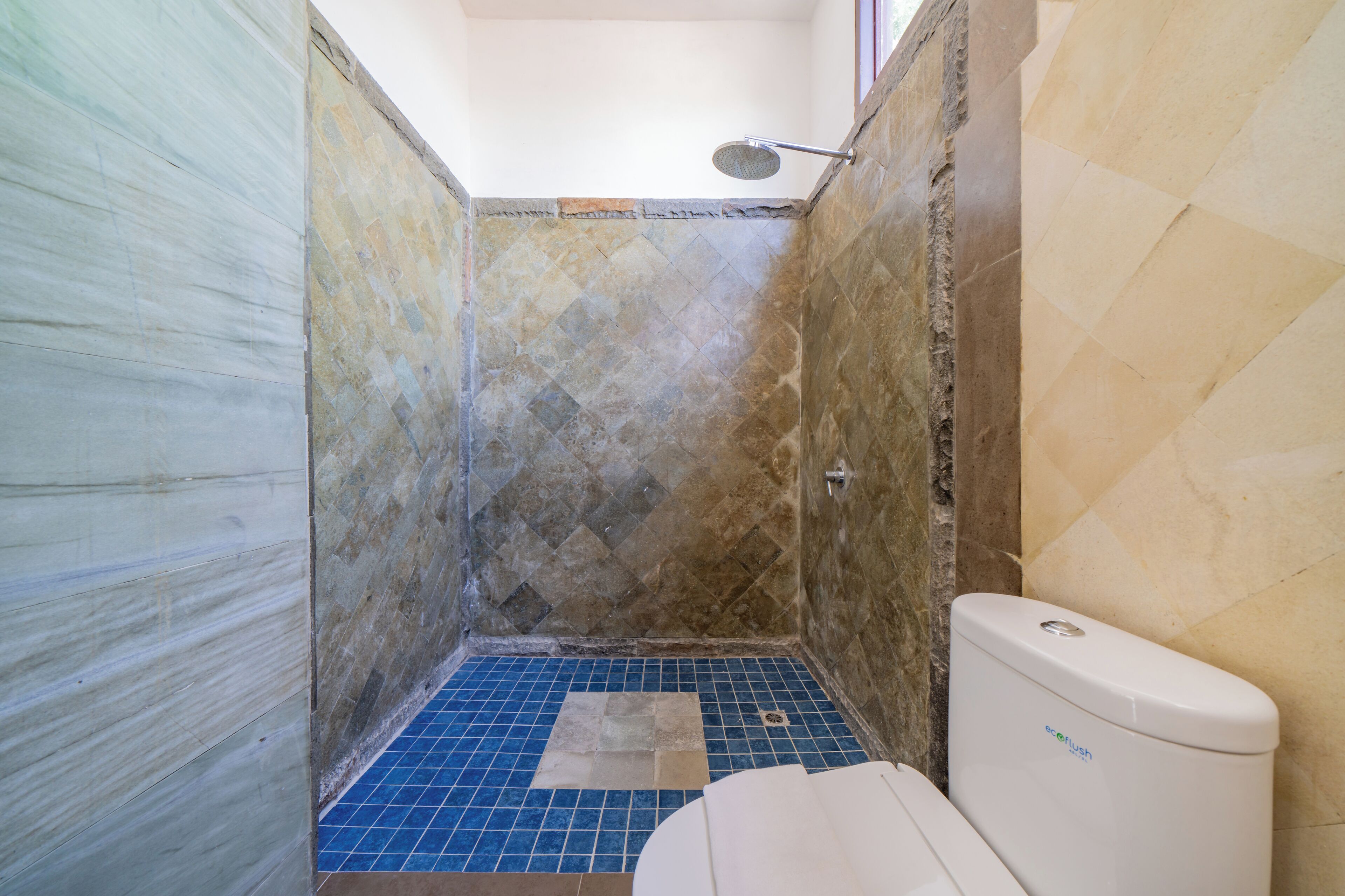 Casa de banho com chuveiro, sanita e chão em azulejos azuis.