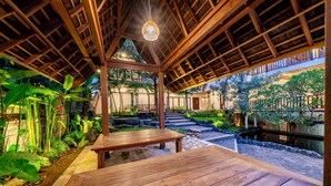 Une terrasse en bois avec un banc, entourée d’une végétation luxuriante et d’un petit étang.
