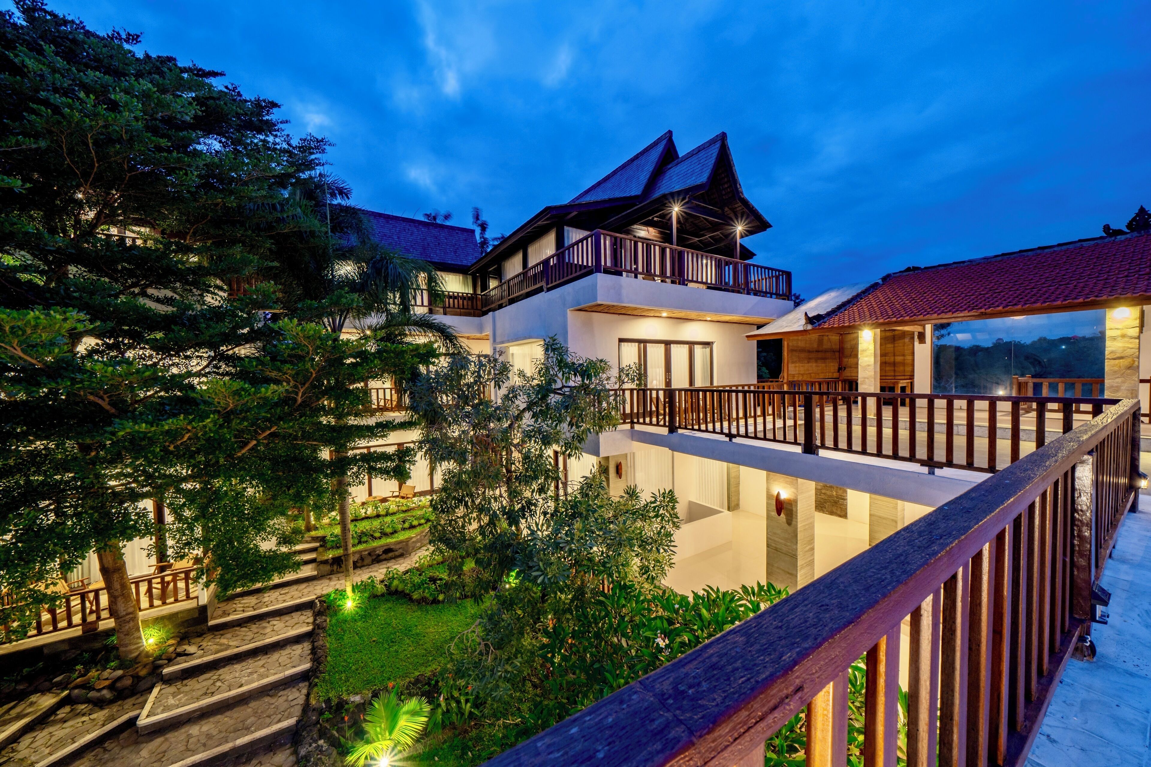 A multi-story building with a balcony, surrounded by lush greenery and stone pathways.