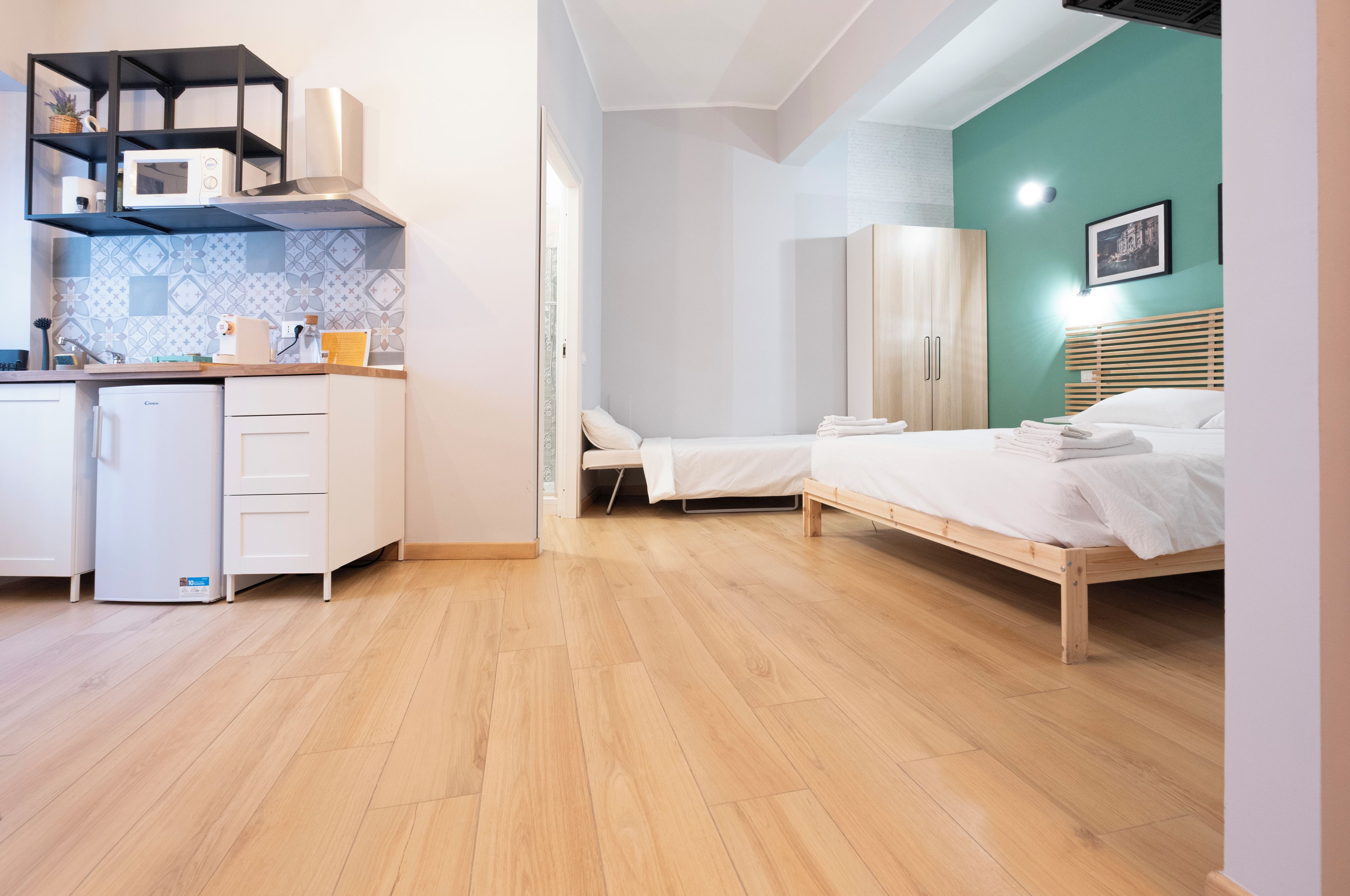 A compact room with a kitchenette, a bed, and a wardrobe.