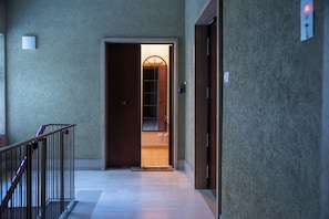 A hallway with a wooden door leading to a room, a handrail on the left, and a wall-mounted light fixture. - Urban House Marconi (Roma)