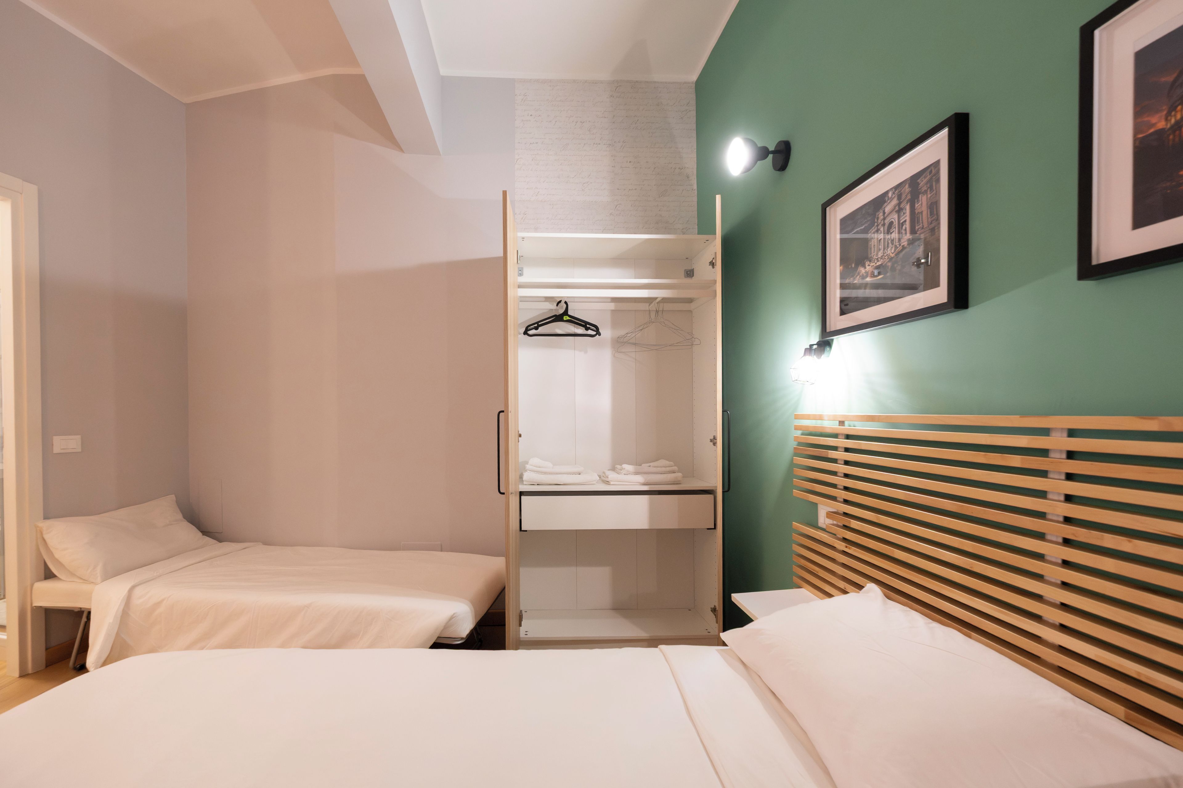 A room with two beds, a wardrobe, and a framed picture on the wall.