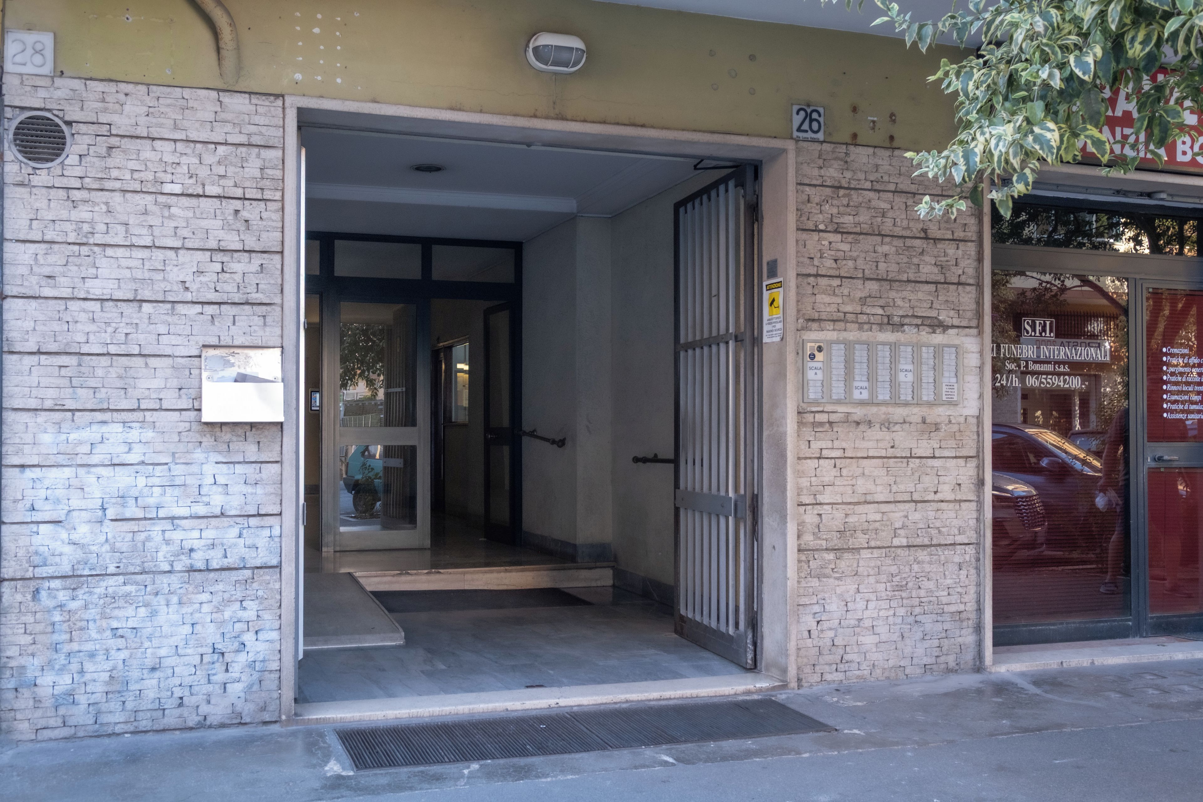 A building entrance with a metal gate, a brick wall, and a door leading inside.