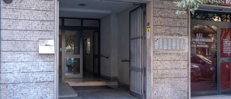 A building entrance with a metal gate, a brick wall, and a door leading inside.