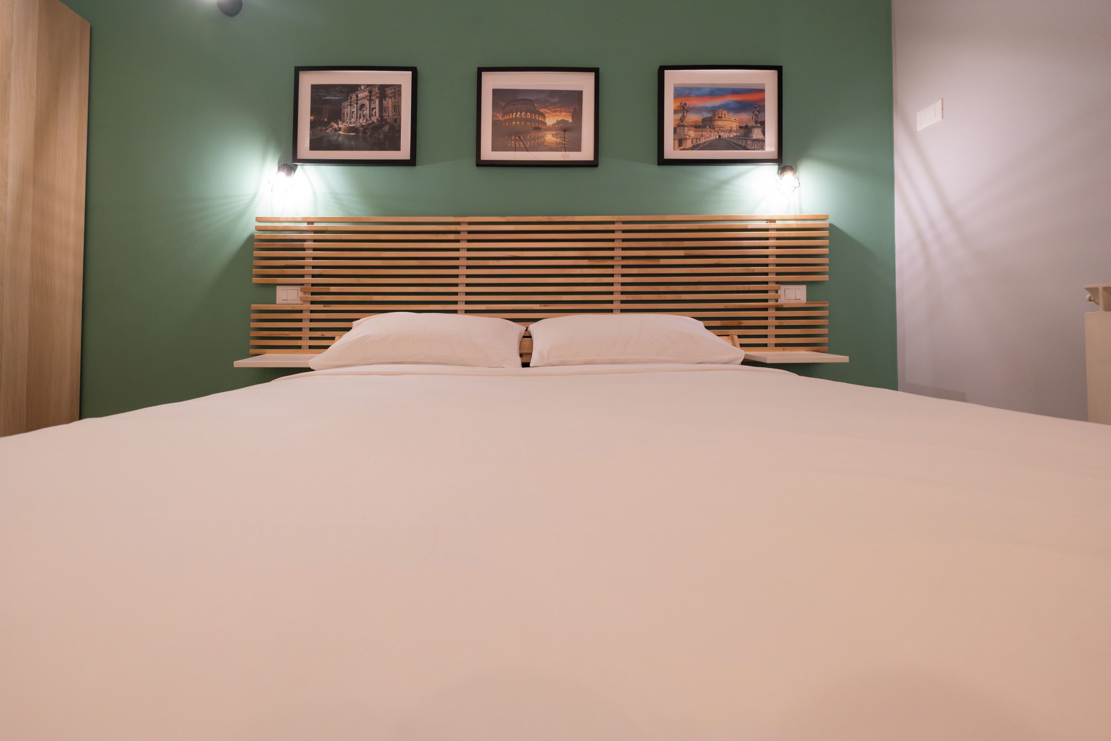 A bed with a wooden headboard, two pillows, and three framed pictures on the wall above.