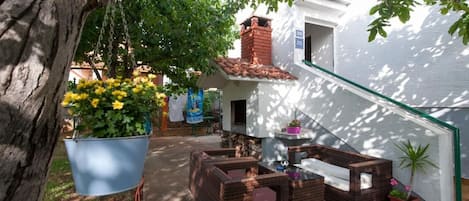A courtyard with wicker furniture, hanging plants, and a white building with a red-tiled roof.