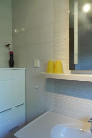 Un baño moderno con un lavamanos blanco, un espejo y una repisa con tazas amarillas.