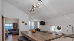 A modern kitchen with a wooden island, bar stools, a flat-screen TV, and a view of the sea. - Apartman Irena by Interhome (Medici)