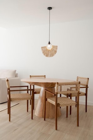 A dining area with a round wooden table surrounded by four woven chairs, a hanging light fixture, and a white wall in the background. - Sunny Oasis Apartment in La Oliva (La Oliva)