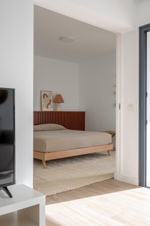 A bedroom with a bed, a bedside lamp, a television on a stand, and a door leading to another room. - Sunny Oasis Apartment in La Oliva (La Oliva)