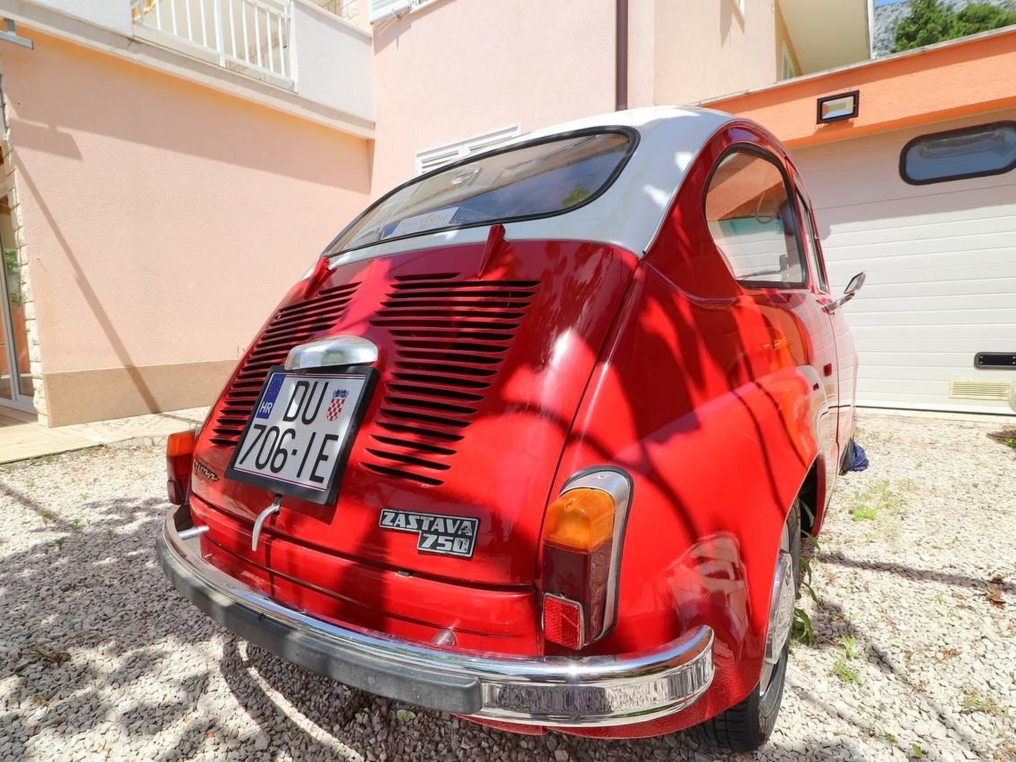A vintage red car parked in front of a house with a garage.