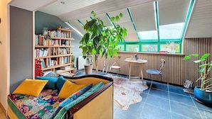 A cozy living room with a bookshelf, a large potted plant, a sofa with colorful cushions, and a skylight. - Étel – 3-room house – 110 m² – WiFi - 3* (ETEL)