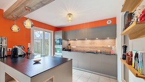 A modern kitchen with a central island, grey cabinets, and orange walls. - Étel – 3-room house – 110 m² – WiFi - 3* (ETEL)