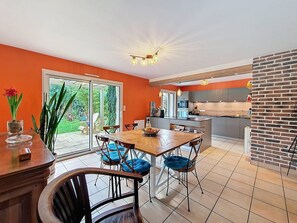 A modern kitchen with an island, a dining area with a wooden table and blue cushioned chairs, and a large sliding glass door leading to a garden. - Étel – 3-room house – 110 m² – WiFi - 3* (ETEL)