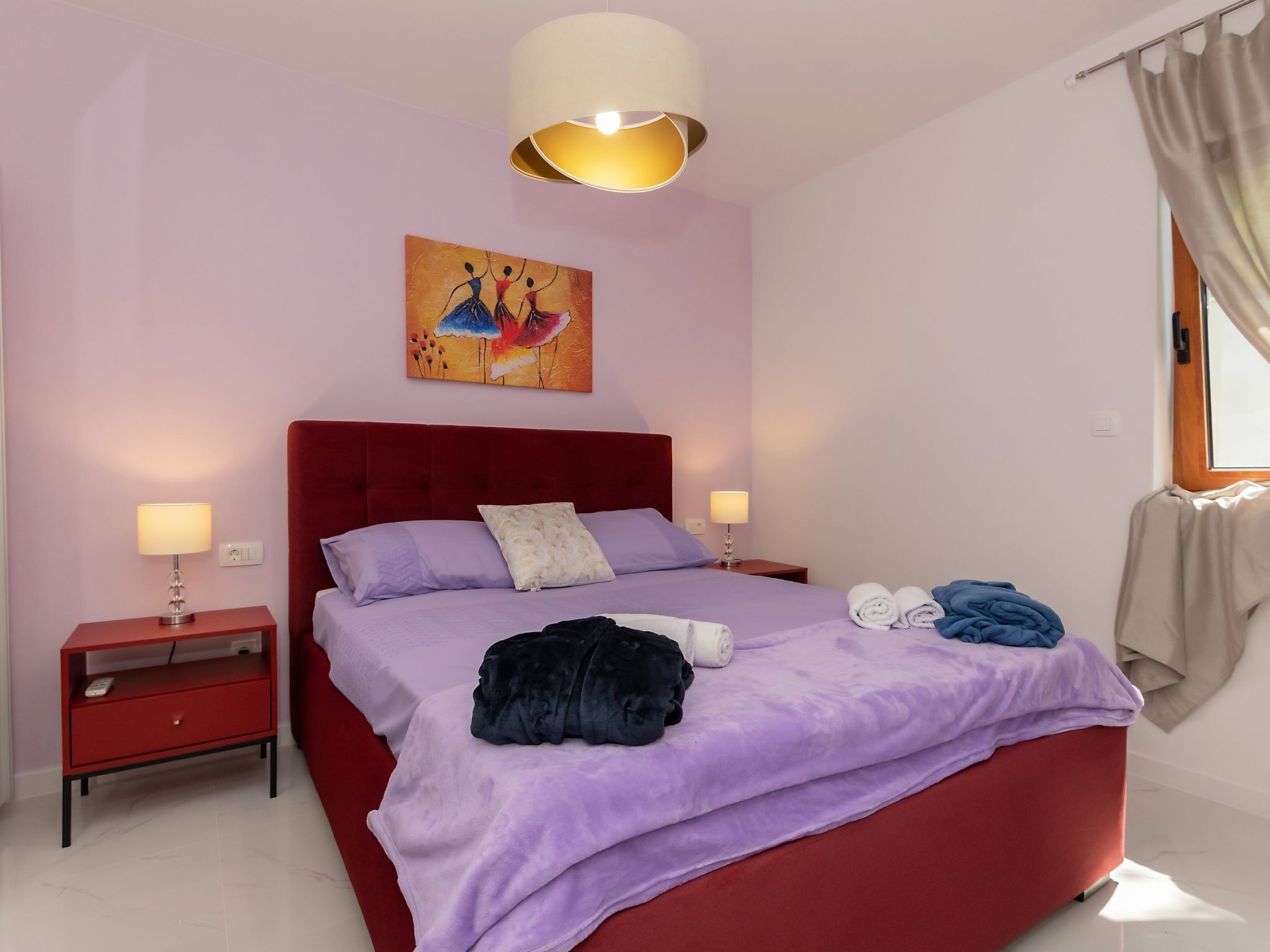 Ein Schlafzimmer mit einem roten Kopfteil, einer violetten Tagesdecke und einem Bild an der Wand.