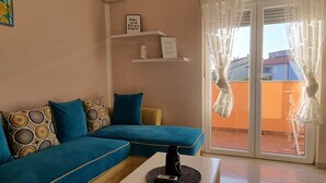 A living room with a blue sofa, patterned cushions, a white coffee table, and a glass door leading to an outdoor area.