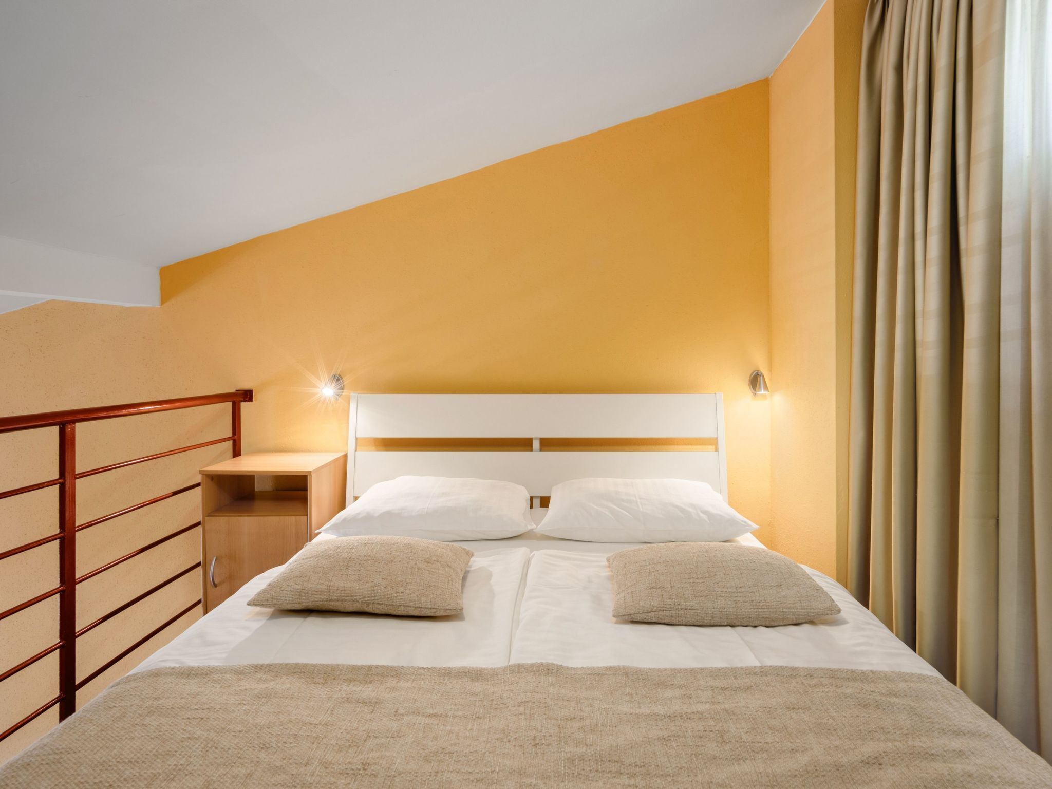 A hotel room with a bed, a nightstand, a wooden headboard, and a curtain.