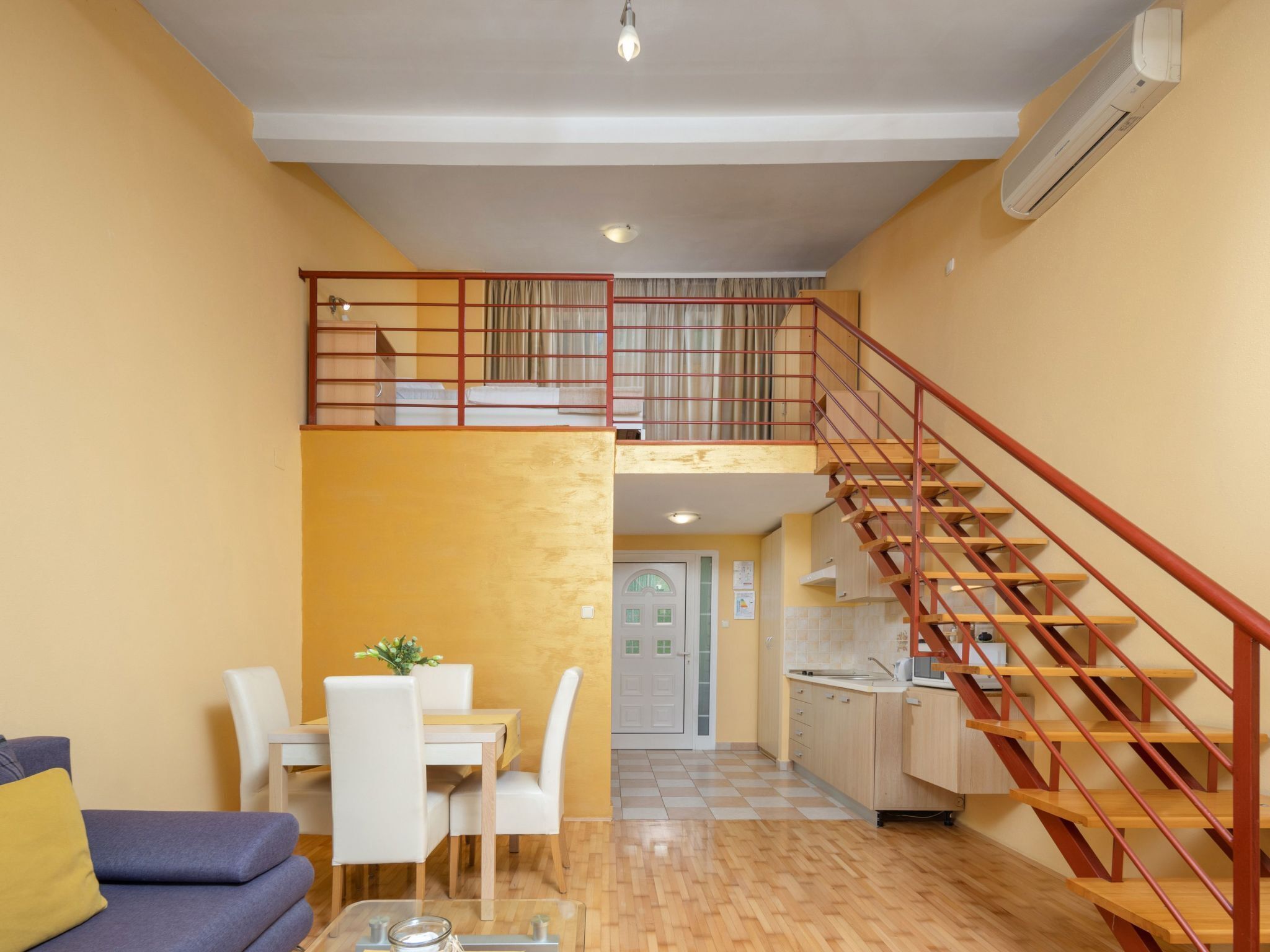 A two-story apartment with a dining area, a sofa, a staircase, and a kitchen.