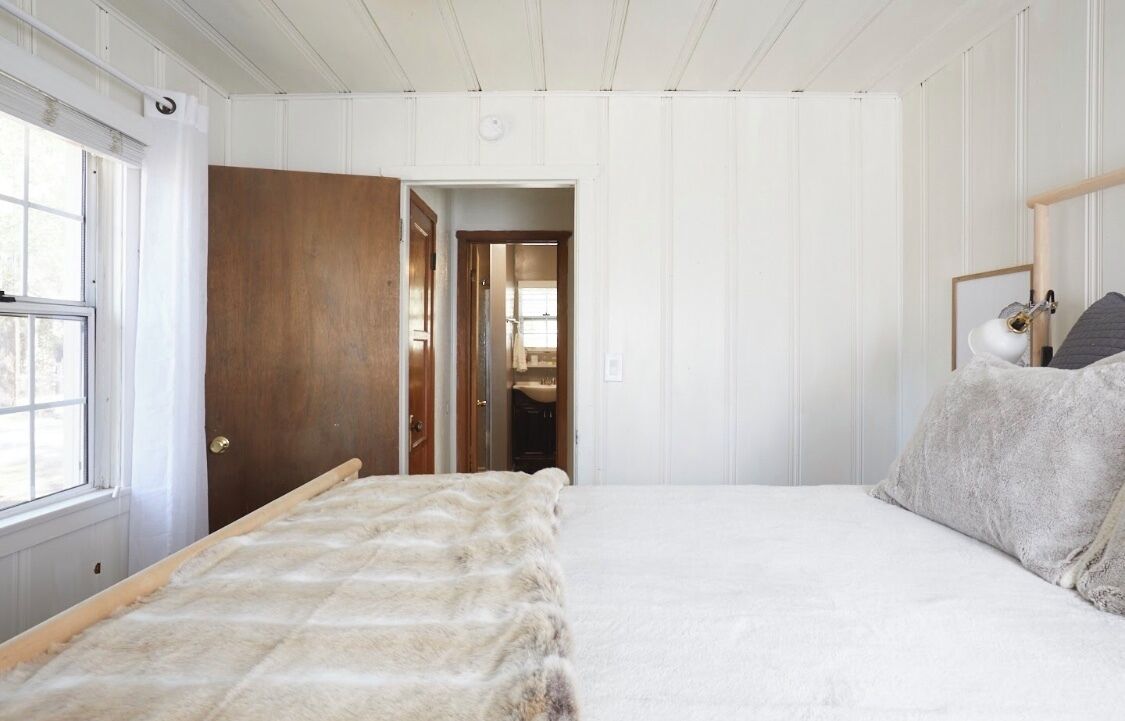 Een slaapkamer met een groot bed, een houten deur en een raam.