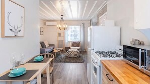 A compact kitchen with a gas stove, microwave, and white cabinets. There is a dining area with a table and chairs, and a cozy seating area with a sofa and cushions.