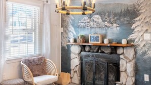 A cozy room with a stone fireplace, a chair with a fur throw, and a view of a snowy landscape through the window.