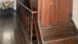 A wooden staircase leading to a landing with a door, a wooden railing, and a flower arrangement on the landing. - Vallée des Prés by Interhome (Mesnil-Saint-Blaise)