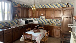 A kitchen with wooden cabinets, a microwave, a sink, and a dining table with chairs. - Vallée des Prés by Interhome (Mesnil-Saint-Blaise)
