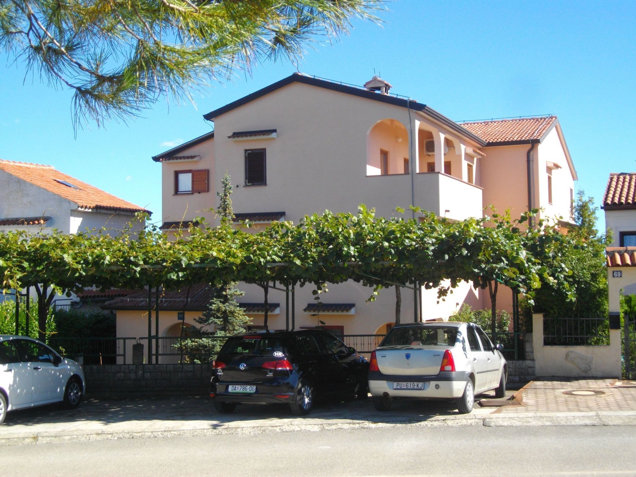 A two-story building with a flat roof and a balcony on the upper floor. There are two cars parked in front of the building.