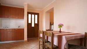 A kitchen with wooden cabinets, a tiled floor, and a dining area with a table and chairs. - 1573593 by Interhome (Poreč)