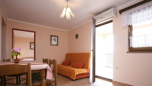 A room with a dining table, chairs, a sofa, a vase with flowers, a ceiling light, and a window with lace curtains. - 1573593 by Interhome (Poreč)