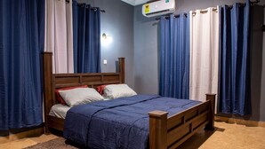 A bedroom with a wooden bed, blue curtains, and an air conditioning unit. - Clean beds, Sound Sleep (Accra)