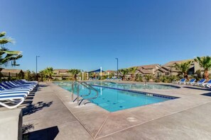 Ein Pool mit blauen und weißen Liegestühlen, blauem Himmel und Wohnhäusern im Hintergrund.