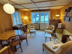 Un salon chaleureux avec des murs en bois, une table à manger, deux fauteuils, un canapé et une bibliothèque.