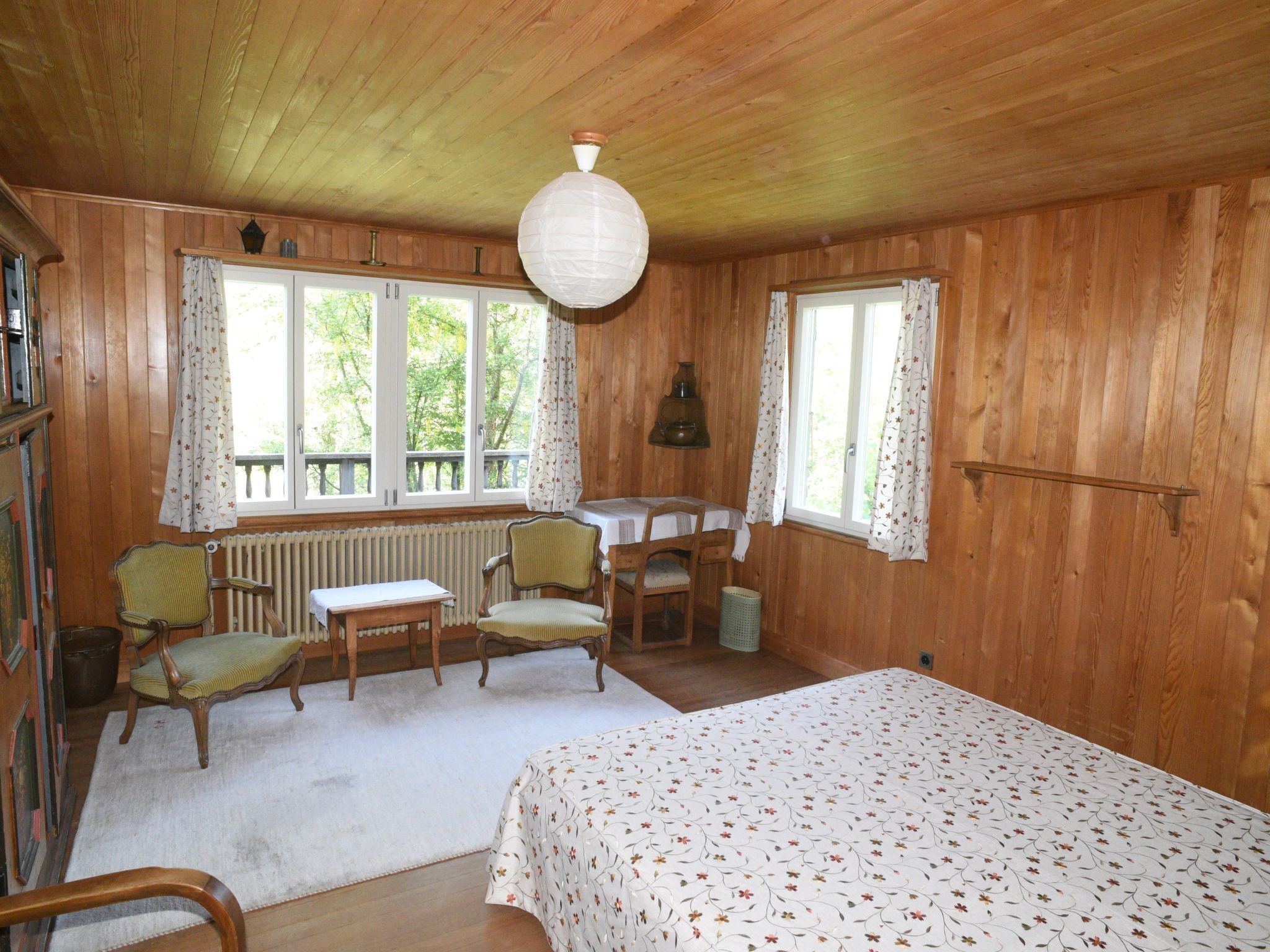 Une pièce de cabane en bois comprenant un lit, deux chaises, une table et un radiateur.