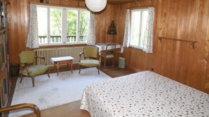 A wooden cabin room with a bed, two chairs, a table, and a radiator.