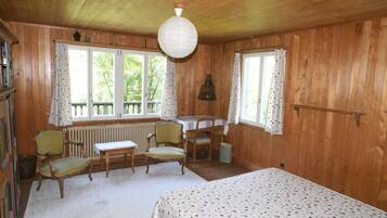 Une pièce de cabane en bois comprenant un lit, deux chaises, une table et un radiateur.