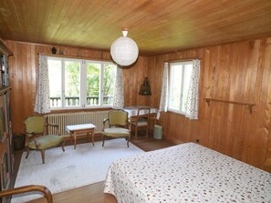 Une pièce de cabane en bois comprenant un lit, deux chaises, une table et un radiateur.
