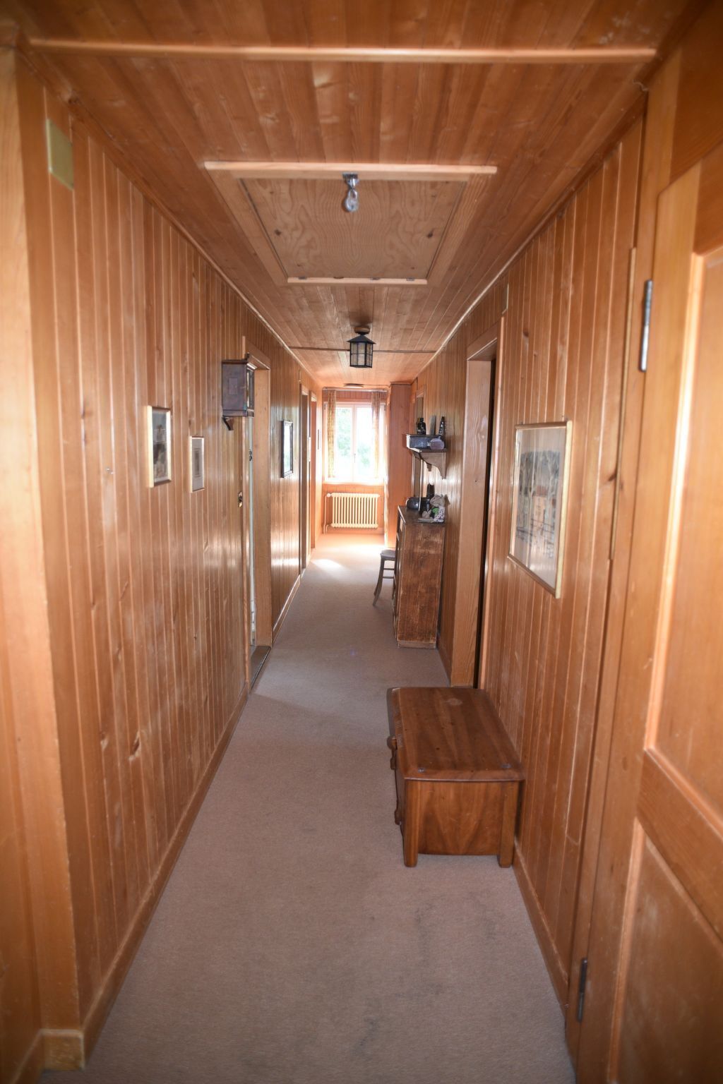 Un couloir en bois avec un banc, des tableaux encadrés et une fenêtre au fond.