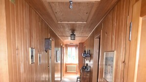 A wooden hallway with a bench, framed pictures, and a window at the end.