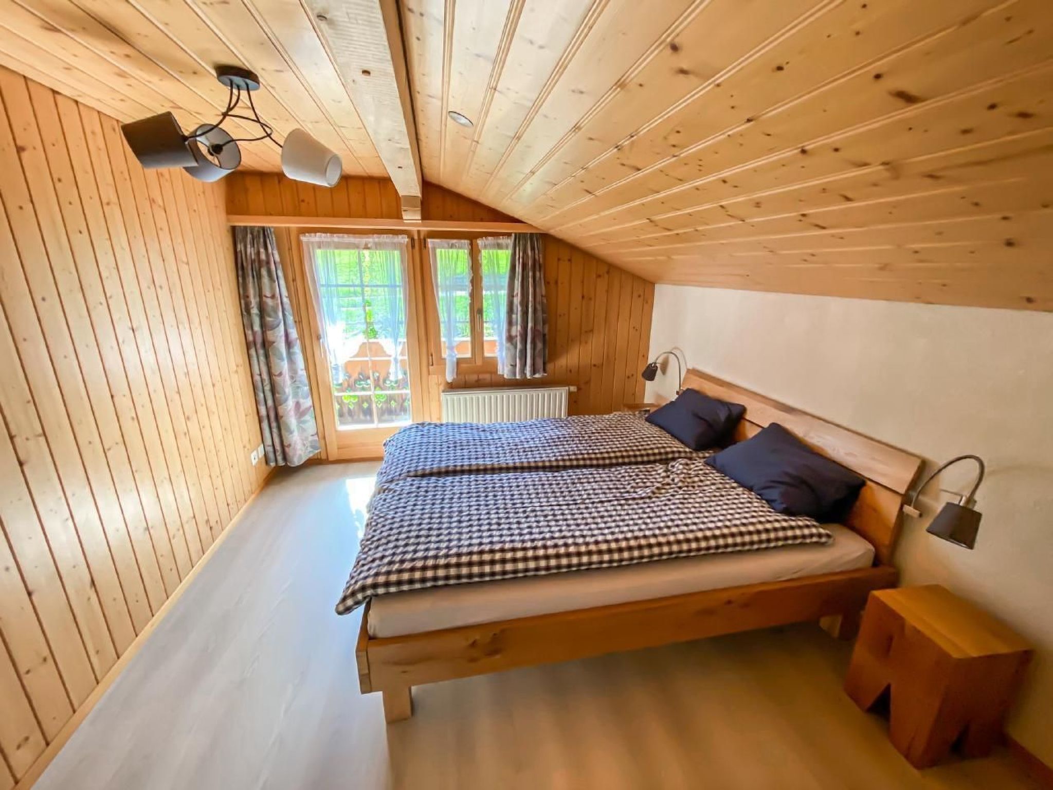 Une chambre à coucher dans un chalet en bois, avec un lit, deux lampes de chevet et une fenêtre avec des rideaux.