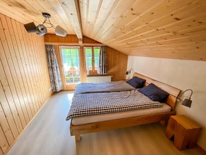 A wooden cabin bedroom with a bed, two bedside lamps, and a window with curtains.