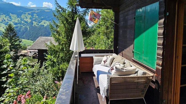A wooden balcony with a wicker sofa, a white umbrella, and a view of a mountain landscape. - Chalet Tannegüetli by Interhome (Grindelwald)