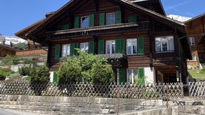 A traditional wooden chalet with multiple windows and a balcony, surrounded by a stone wall and greenery. - Chalet Fluehbluemli / Eigerview by Interhome (Grindelwald)