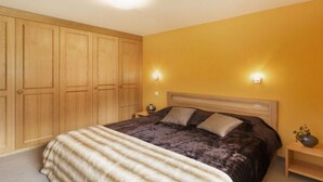 Un dormitorio con cama, armario de madera y dos lámparas de noche.