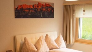 Ein Schlafzimmer mit Bett, Nachttisch, Lampe, Gemälde und einem Fenster mit Vorhängen.