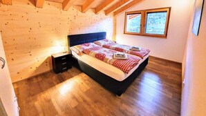 A bedroom with a wooden ceiling, a bed with a checkered blanket, a nightstand, and a window with a view of the outdoors.