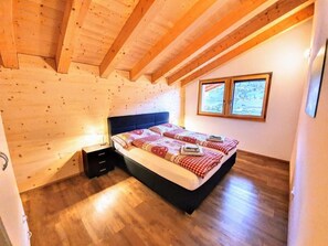 A bedroom with a wooden ceiling, a bed with a checkered blanket, a nightstand, and a window with a view of the outdoors. - Chalet Eigernordwand by Interhome (Grindelwald)