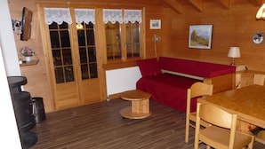 Een knus vertrek met een houten vloer, een rode bank, een houten tafel met stoelen, en een klein rond tafeltje.