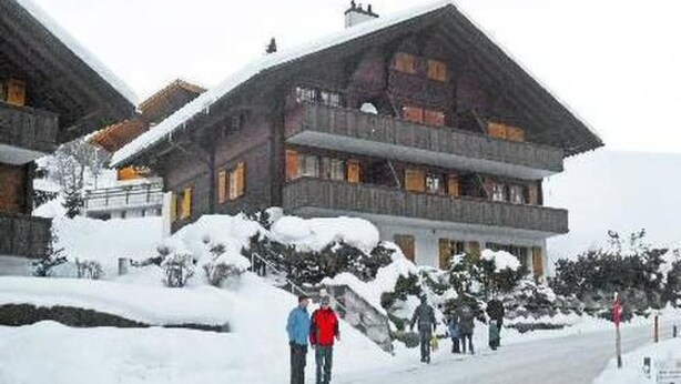 Een klassiek houten chalet met een steil dak, meerdere ramen en een met sneeuw bedekte grond.